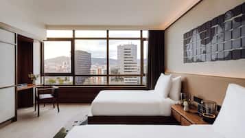 Habitación de hotel moderna con un ventanal grande, una cama, un escritorio y vistas a la ciudad.