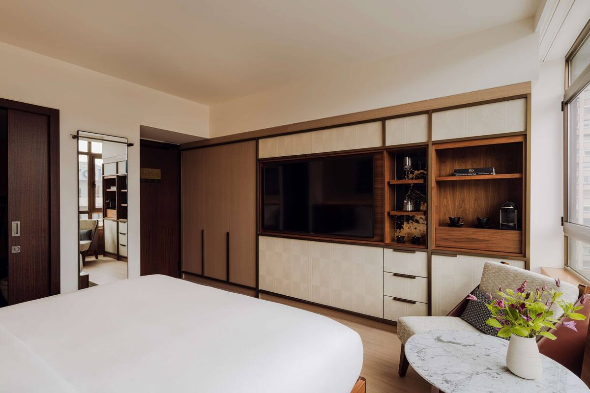 Une chambre moderne avec un grand lit, une télévision et un coin salon agrémenté d’un vase de fleurs.