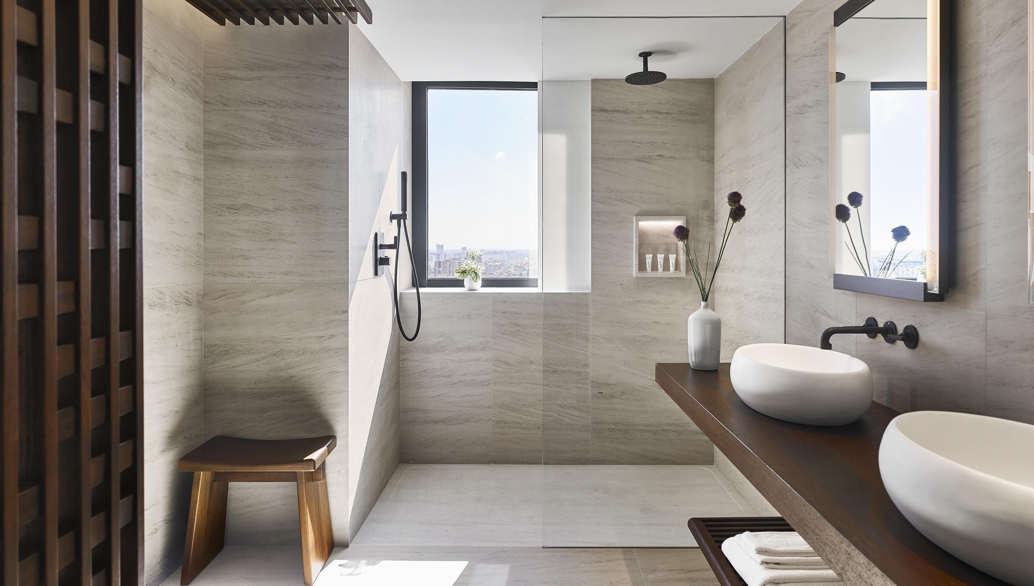 A modern bathroom with a large window, a shower, a vanity with a sink, and a small stool.