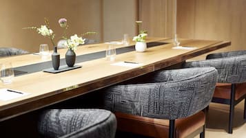 A conference room with a long table, grey upholstered chairs, and vases with flowers.