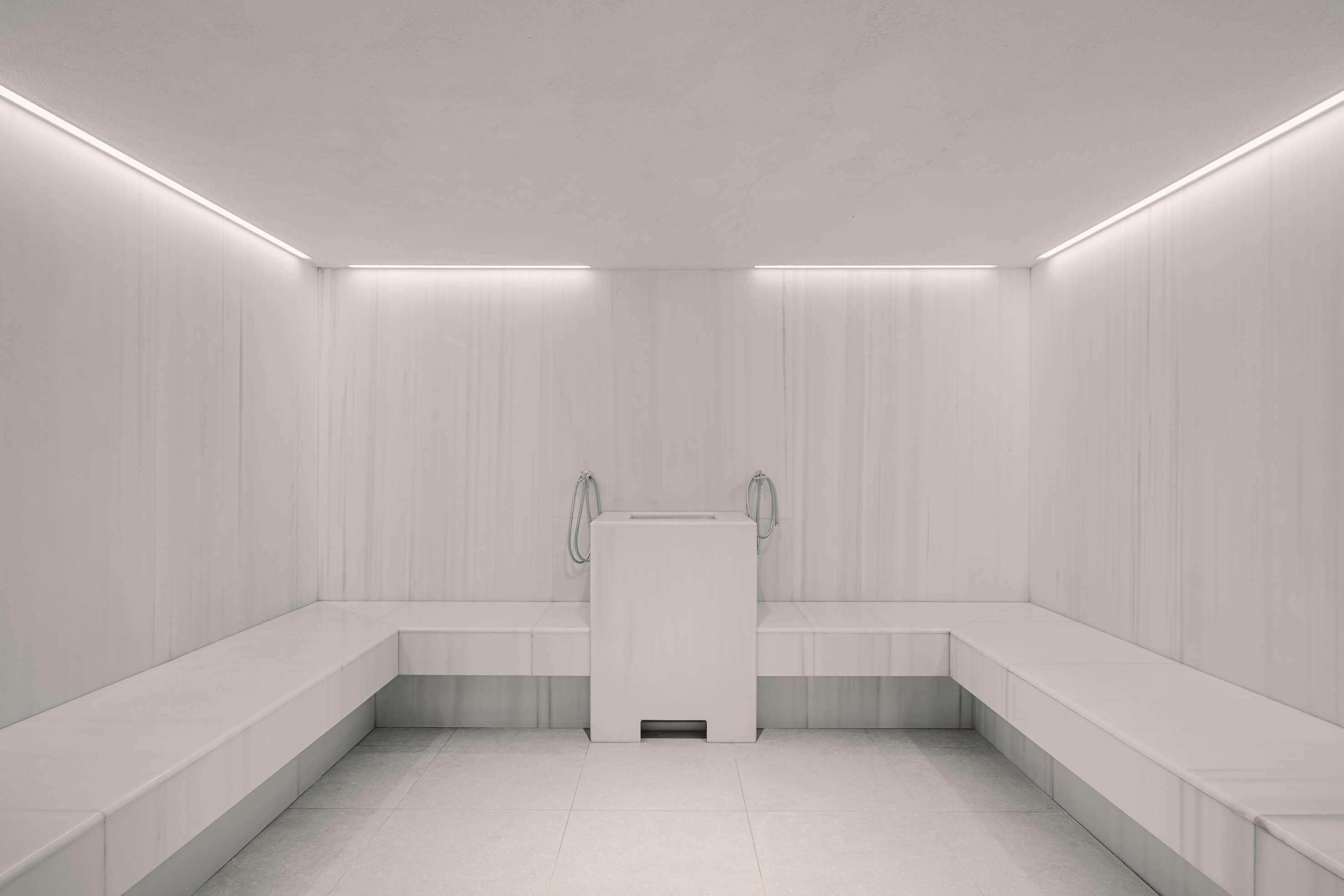 Um banheiro moderno e minimalista, com área de chuveiro central, bancos ao longo das paredes e iluminação embutida.