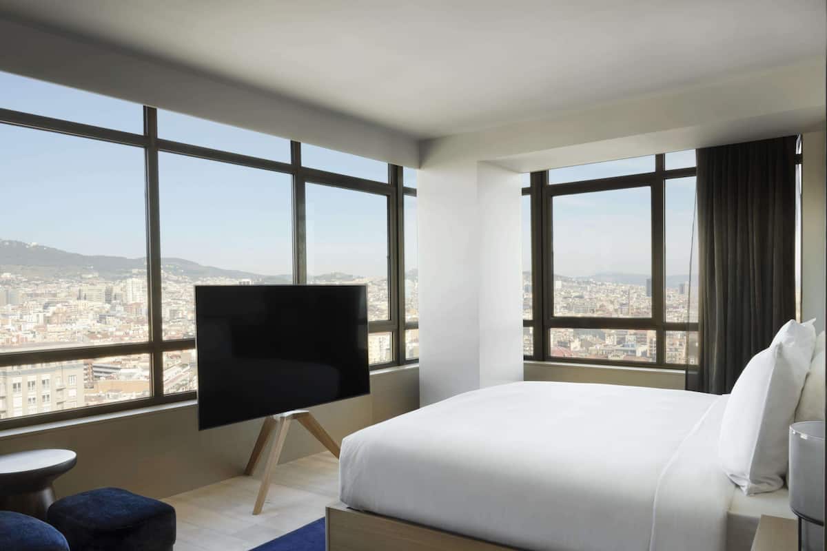 Une chambre d’hôtel moderne dotée d’un grand lit, d’un téléviseur à écran plat et offrant une vue sur la ville grâce à de grandes fenêtres.