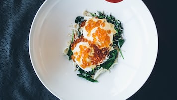 Un plato blanco con una porción de fideos, verduras y un huevo escalfado cubierto de caviar.