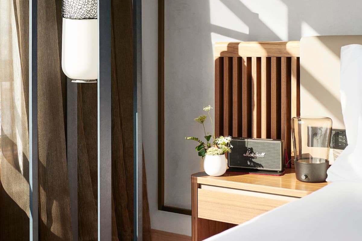 Une chambre d’hôtel avec un lit, une table de chevet sur laquelle se trouve un haut-parleur Marshall, une petite plante et une machine à café.
