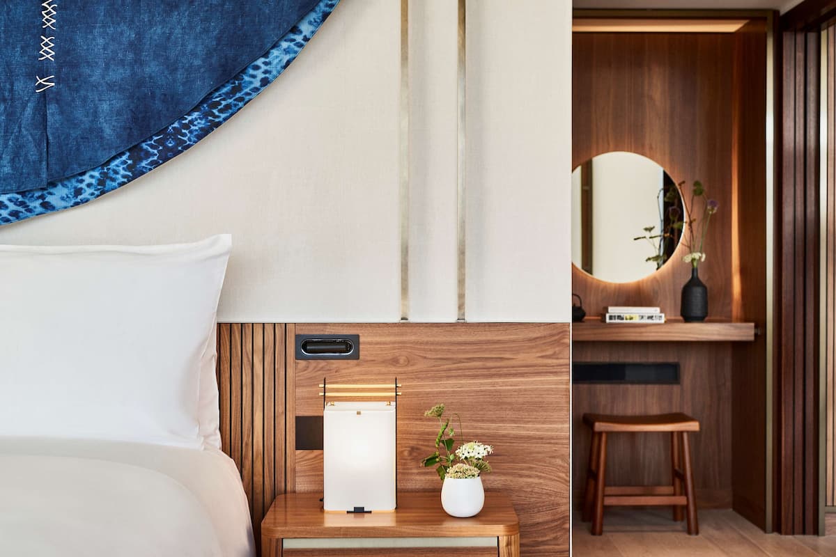 Une chambre à coucher avec un lit, une table de chevet avec une lampe et une petite plante, une commode en bois et un miroir.