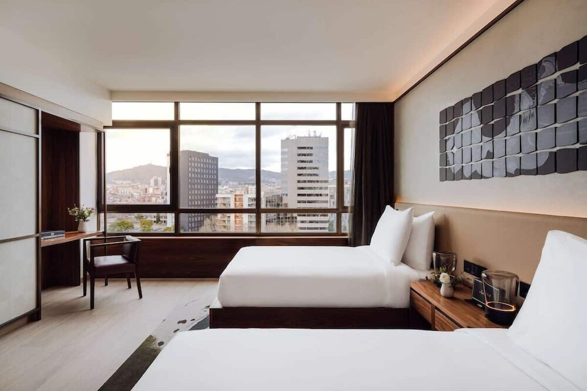 Une chambre d’hôtel moderne avec une grande fenêtre, un lit, un bureau et une chaise.