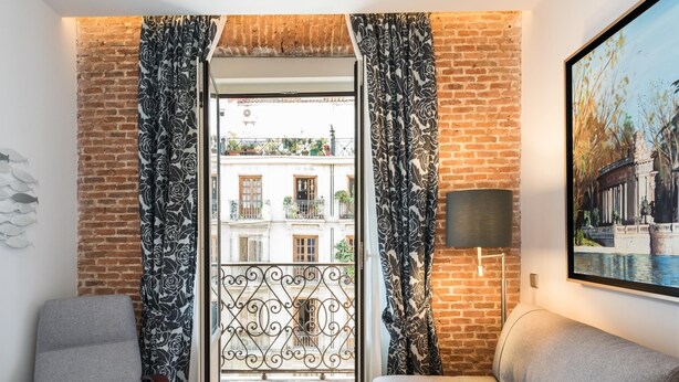 Ein Zimmer mit Blick auf ein Gebäude durch eine Glastür, eine Couch, eine Lampe und ein Gemälde an der Wand.