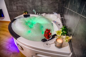 A spa tub with bubbles, a glass of wine, and flowers.
