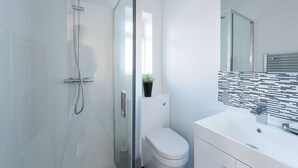 A modern bathroom with a glass shower enclosure, a white toilet, and a sink with a tiled backsplash. - Spectacular Modern Apartment (5 mins to tube) (Greater London)