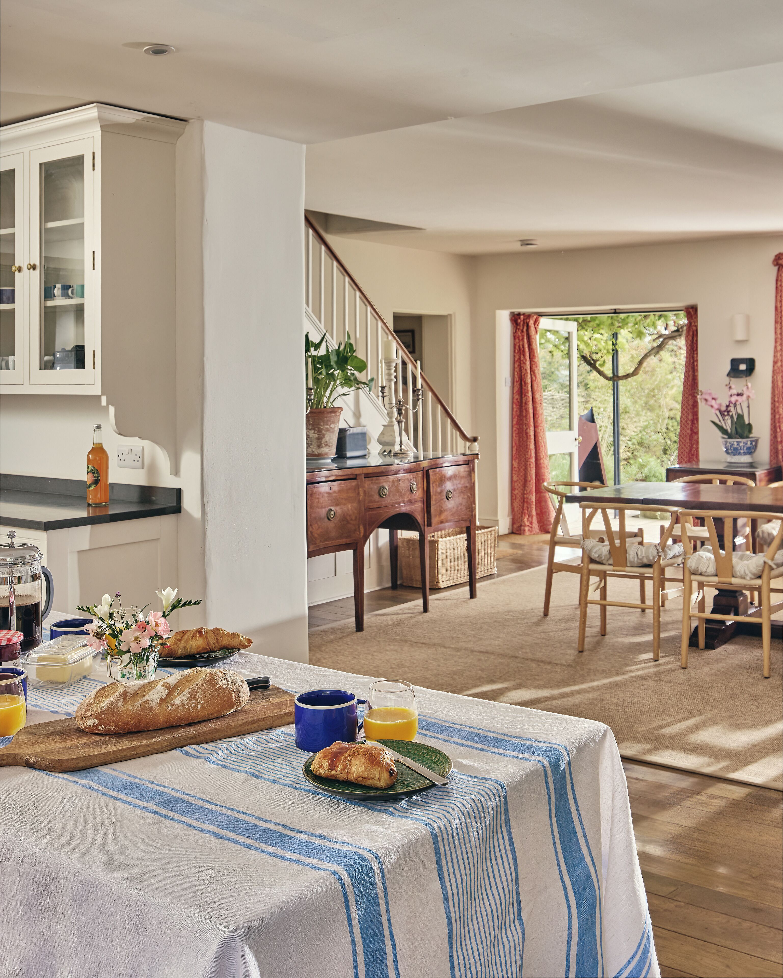 Un coin repas avec une table mise pour le petit-déjeuner, comprenant du pain, des viennoiseries et une carafe de jus d’orange.