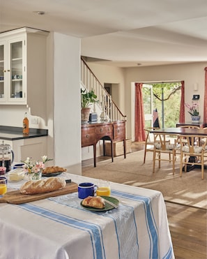 Un coin repas avec une table mise pour le petit-déjeuner, comprenant du pain, des viennoiseries et une carafe de jus d’orange.