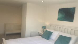 Een slaapkamer met een wit bed, twee turquoise kussens, een witte nachtkastje met een lamp, en een witte radiator.