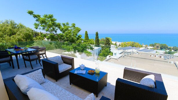 A rooftop terrace with wicker furniture, a table with a teapot, and a view of the sea and buildings. - Villa Panorama (La Marsa)