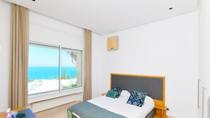 A hotel room with a bed, a nightstand, a window with a view of the sea, and a thermostat on the wall. - Villa Panorama (La Marsa)