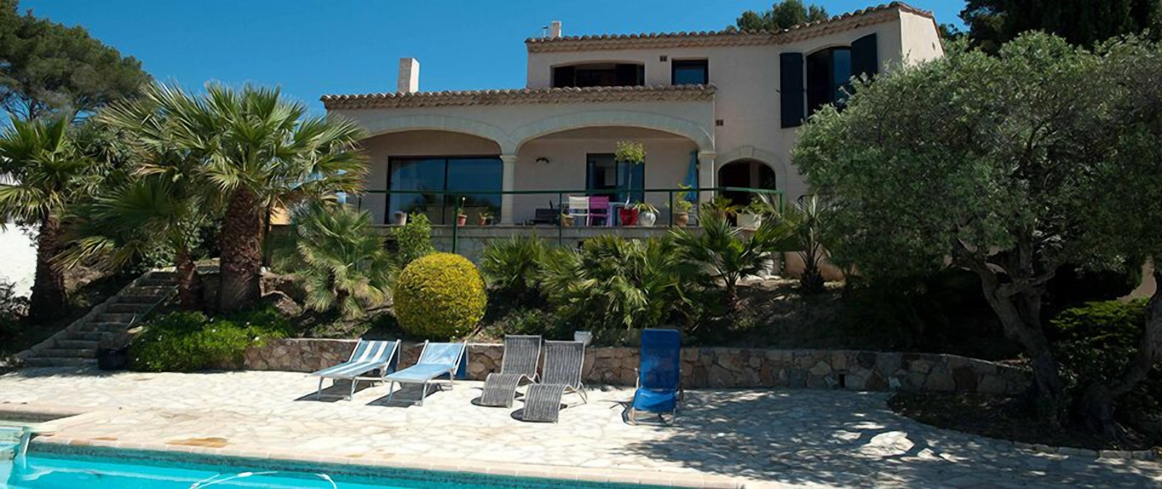 A two-story house with a swimming pool, lounge chairs, and a well-maintained garden.