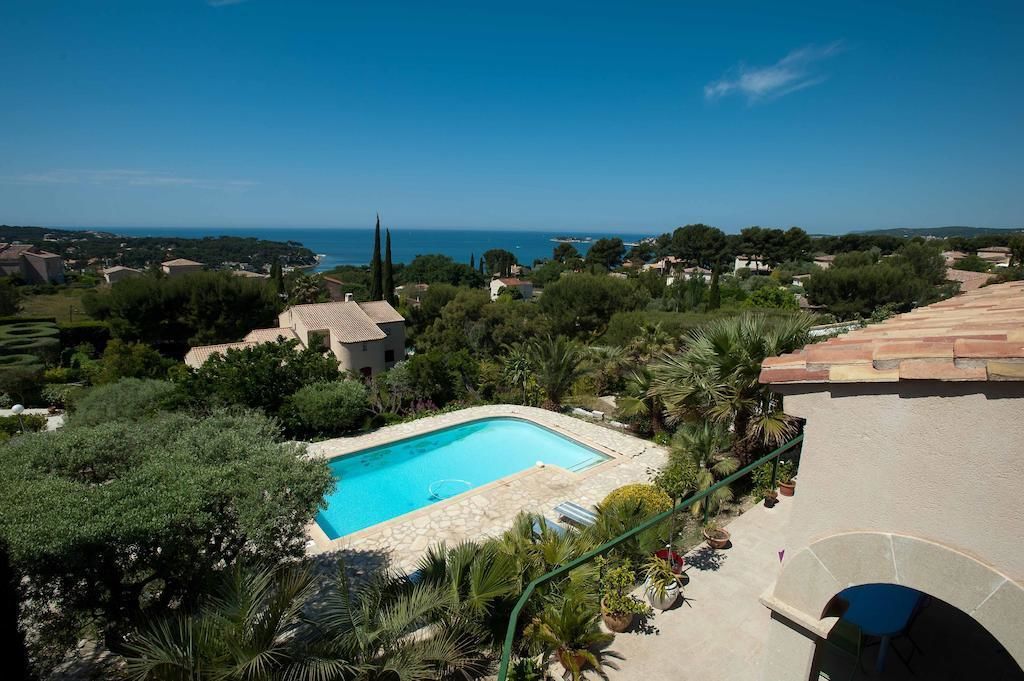 Une piscine entourée de verdure et de maisons, avec une vue dégagée sur la mer en arrière-plan.
