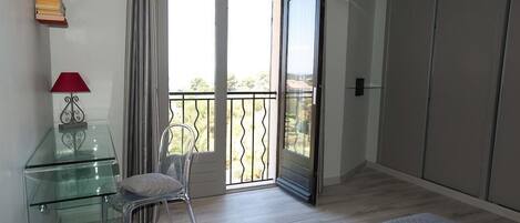 Una habitación moderna con un escritorio de vidrio, una silla, una lámpara roja y un puertas correderas de vidrio que dan a un balcón.