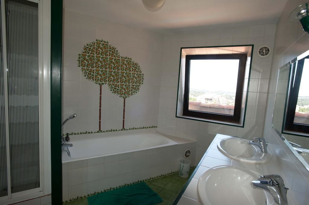 A bathroom with a bathtub, two sinks, a window with a view, and a decorative tree mural on the wall.