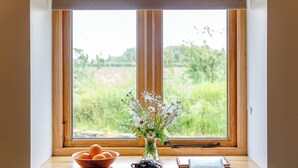 Una finestra con vista sul verde, una ciotola di arance, un vaso con fiori e un libro sul davanzale.