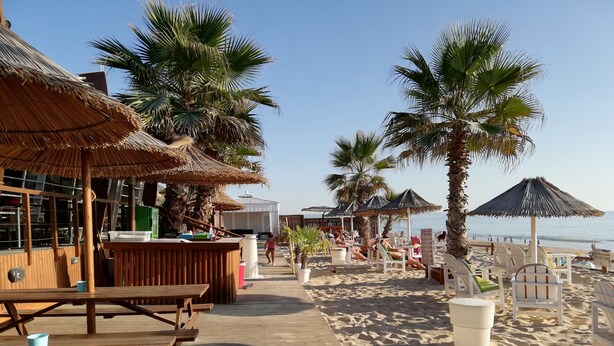 A beachside restaurant with outdoor seating, palm trees, and a wooden deck leading to the beach. - Casa da Vista Rio  (Amora)