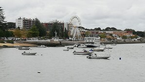 A marina with several boats docked, a Ferris wheel in the background, and buildings along the waterfront. - Casa da Vista Rio  (Amora)