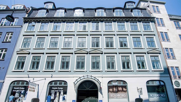 En historisk bygning med en midterindgang, store vinduer og butikker på begge sider.