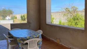 A patio with a round table and chairs, large windows, and a view of greenery and buildings. - Single villa with garden 1300 meters from the sea (Mazara del Vallo)