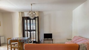 A bedroom with a bed, a TV, a table with chairs, and a window with curtains. - Single villa with garden 1300 meters from the sea (Mazara del Vallo)