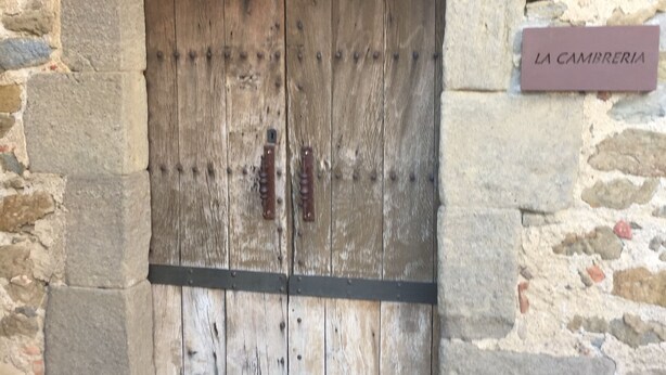 Een houten deur in rustieke stijl, met een stenen muur en een bord waarop 'LA CAMBRERIA' staat.