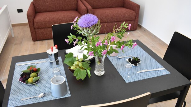Une table à manger dressée avec un panier de fruits, un vase de fleurs et une tasse.