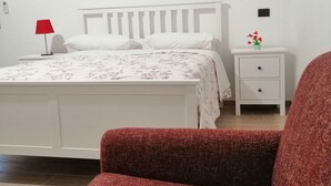 Une chambre à coucher avec un lit, une table de chevet, une lampe et une petite table ornée d’un vase de fleurs.