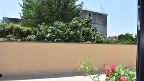 Une terrasse sur le toit avec un mur de couleur beige, un feuillage verdoyant et des fleurs roses.