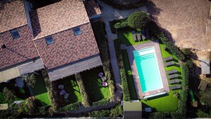 An aerial view of a residential property with a swimming pool, multiple patios, and a well-maintained garden.