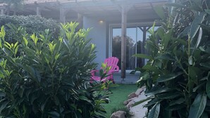 A garden pathway leading to a covered patio area with a pink chair and a pergola.
