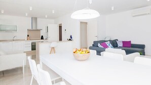 Een moderne, minimalistische woonruimte met een keuken, een eetgedeelte en een grijze bank met kleurrijke kussens.