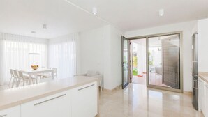 Een moderne keuken met witte kasten, een eethoek met een tafel en stoelen, en een schuifdeur naar een balkon.