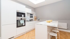 Een moderne keuken met witte kastjes, een inbouwoven, een magnetron en een marmeren aanrecht.