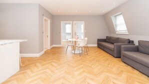 Een ruime woonkamer met een visgraat parketvloer, een grijze bank en een eettafel met stoelen.