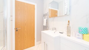 Een moderne badkamer met een houten deur, een wit wastafelmeubel, een spiegel en toiletartikelen op het aanrecht.