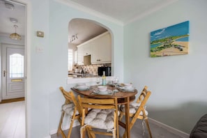 Een eethoek met een ronde tafel, houten stoelen en uitzicht op de keuken door een boog.