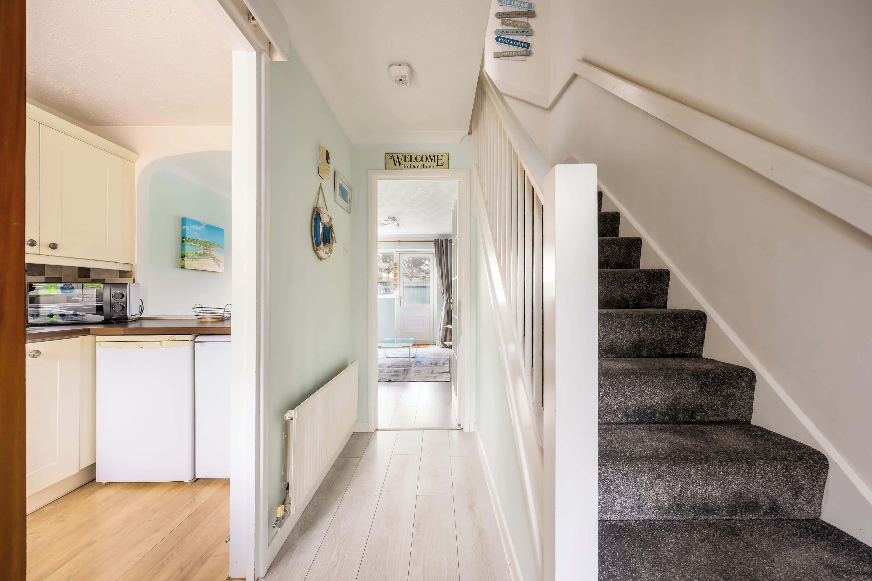 A hallway with a staircase, a kitchen area, and a welcome sign.