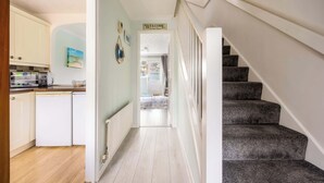 A hallway with a staircase, a kitchen area, and a welcome sign. - Dolphin Cottage  - Short walk to Poole Quay (Poole)