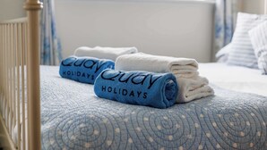 A bed with a blue quilt and rolled towels with 'Quay Holidays' text. - Dolphin Cottage  - Short walk to Poole Quay (Poole)