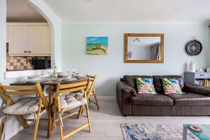 Een eetgedeelte met een houten tafel en stoelen, een bruine leren bank, een schilderij, een spiegel en een klok aan de muur.