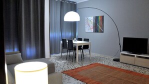 A modern living room with a dining area, a TV, and a large floor lamp. - CASA ROSETTA Palermo Mondello (Palermo)
