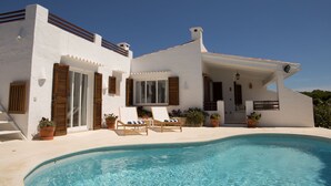 A modern villa with a swimming pool, wooden shutters, and outdoor seating.