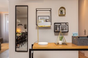 A modern living room with a dining area, a large mirror, a floor lamp, a small potted plant, and framed pictures on the wall.
