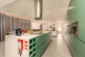A modern kitchen with green cabinets, a stainless steel range hood, and a white countertop.