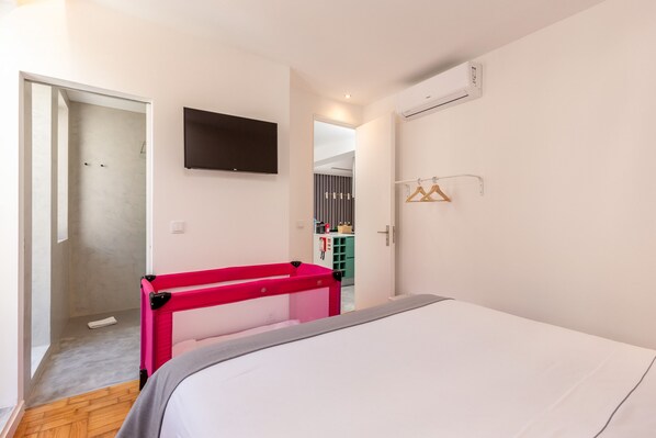 A hotel room with a bed, a TV mounted on the wall, a wardrobe with a mirror, and a door leading to a bathroom.