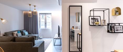 Una sala moderna con un sofá gris, un área de comedor con un espejo, y una cocina al fondo.